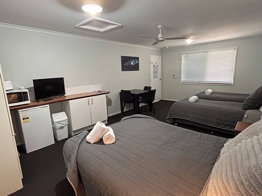 A compact hotel room with a bed, a desk with a computer, a microwave, and a ceiling fan.
