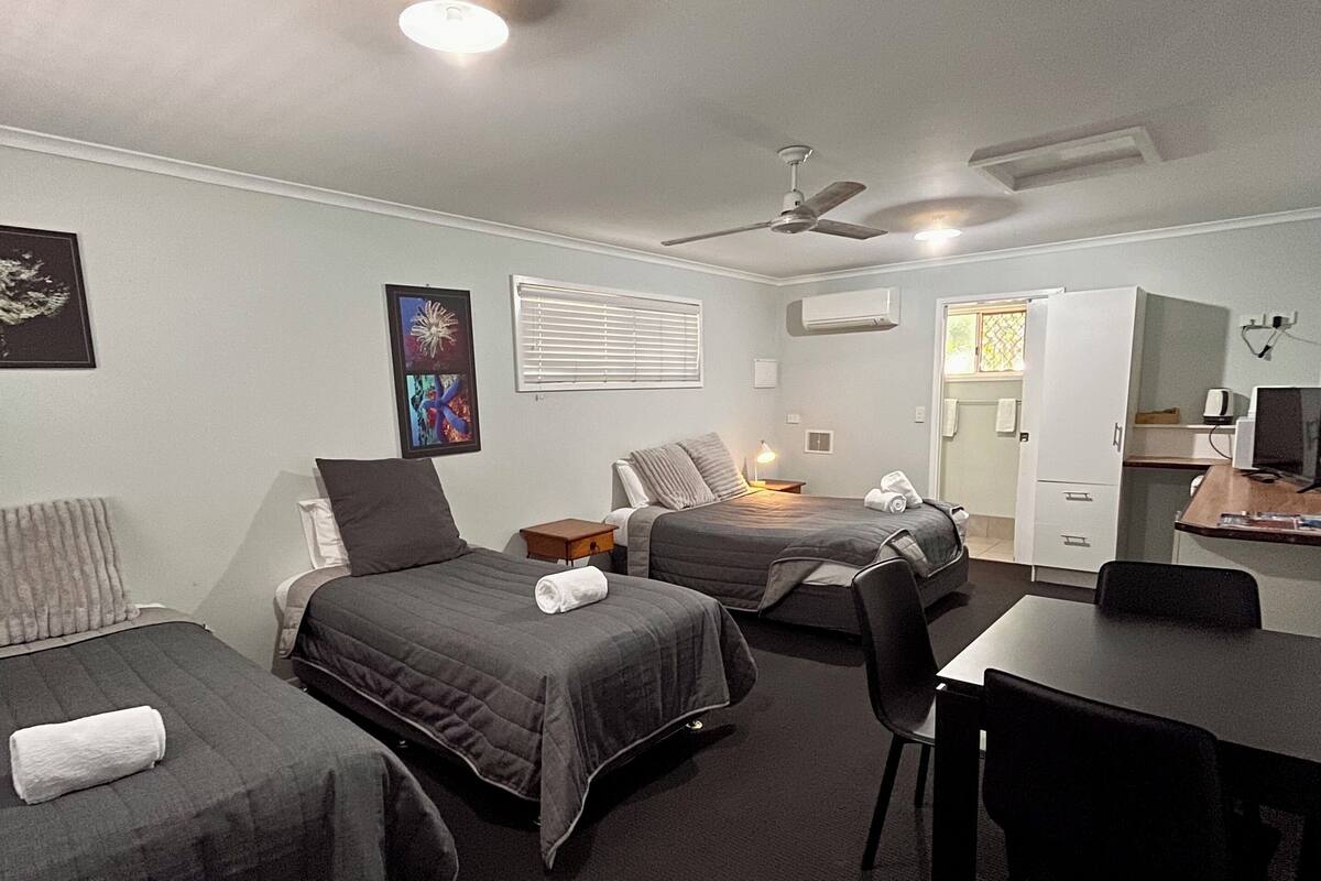 A hotel room with two beds, a desk, a chair, a ceiling fan, and a TV.