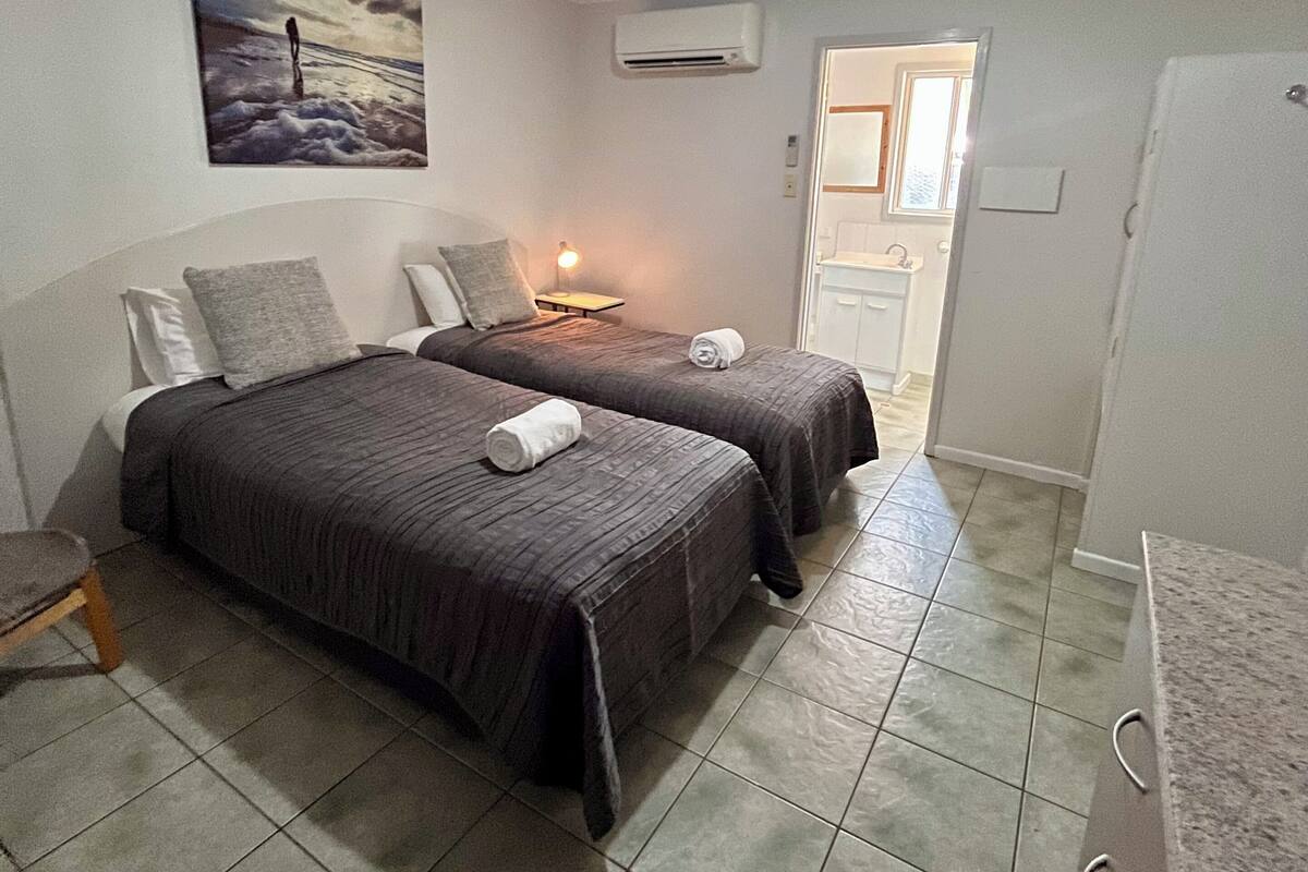 A room with two beds, a painting on the wall, an air conditioner, and a door leading to a bathroom.