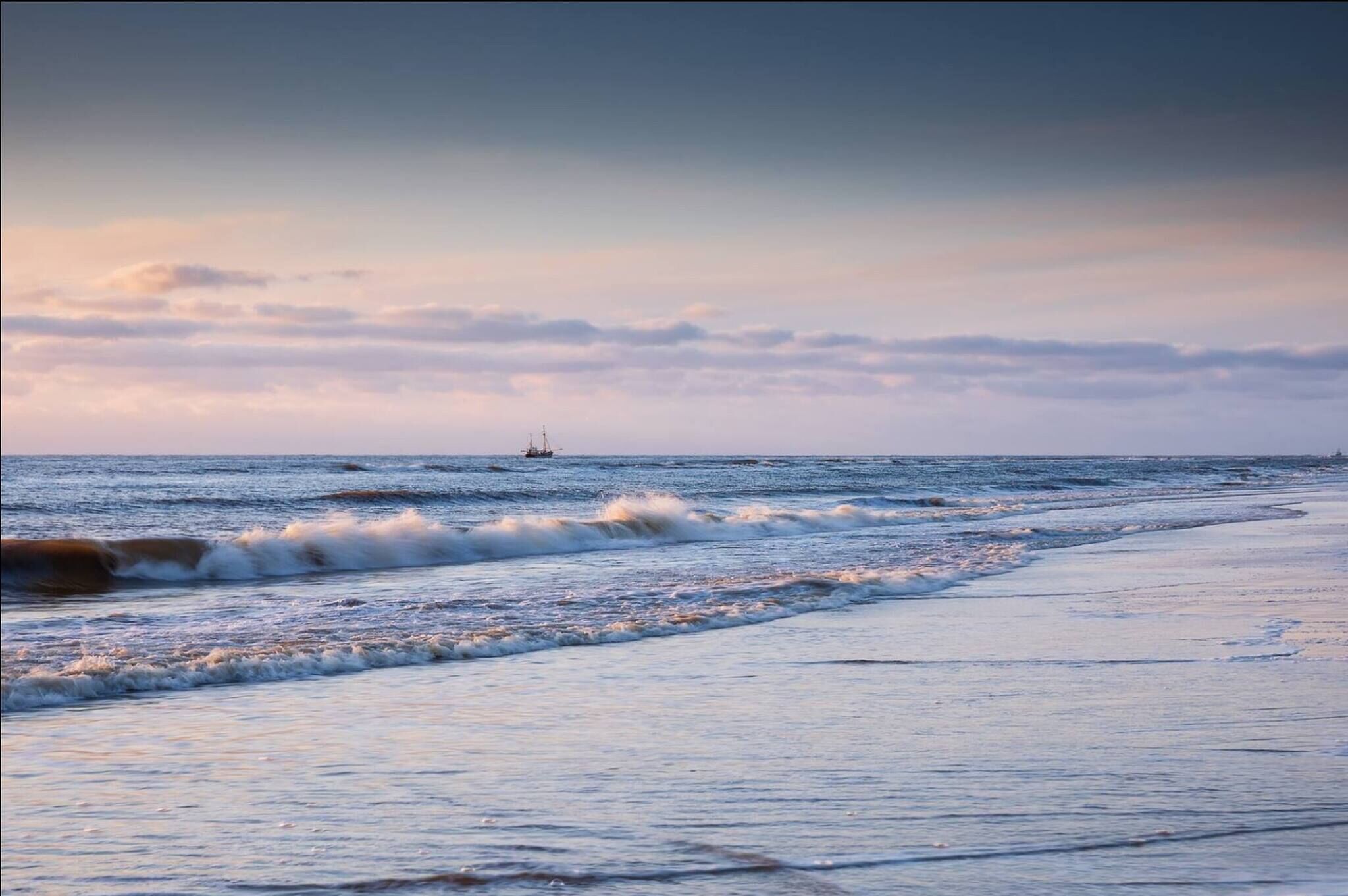 A beach with waves and a distant ship.