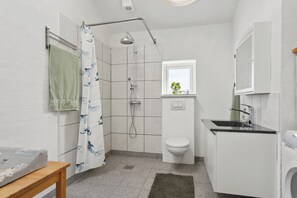 Ein Badezimmer mit Dusche, Toilette, Waschbecken und einem kleinen Fenster mit Pflanze.