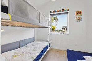 Ein Schlafraum mit Etagenbetten und einem Fenster, einem Bett mit Blumenmuster und einem blauen Sofa.