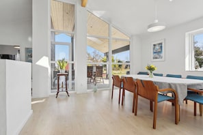 A modern dining area with a large table, chairs, and a view through glass doors.