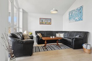 A modern living room with a black leather sofa, a wooden coffee table, and a large abstract painting on the wall.
