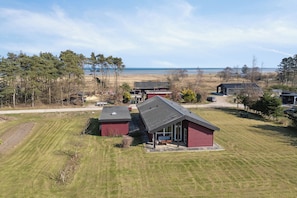 A residential area with a house featuring a covered porch, a lawn, and a view of the beach.