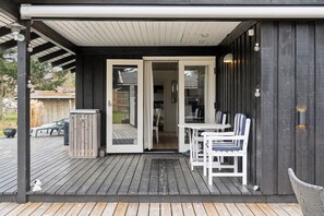 A wooden deck with a covered patio area, a white table with chairs, and a sliding glass door leading to an interior space.