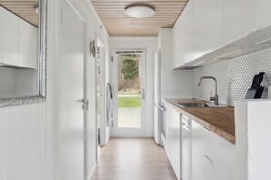 Een moderne keuken met witte kasten, een houten aanrechtblad en uitzicht door een open deur.