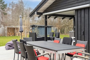 An outdoor patio with a table and chairs, a covered seating area, and a wooden deck.