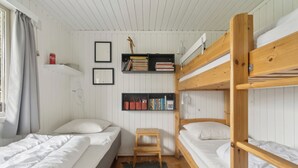 A bunk bed room with a small wooden stool, a shelf with books and baskets, and a window with curtains.