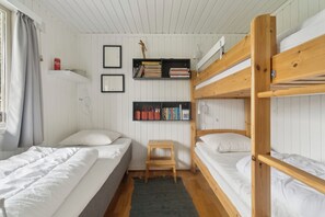 Een slaapkamer met een stapelbed, een klein houten krukje, een plank met boeken en manden, en een raam met gordijnen.