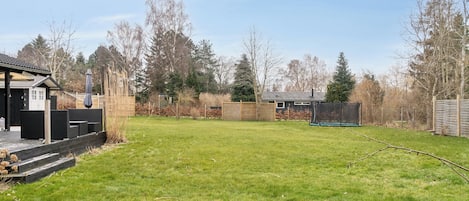 Un jardin avec une terrasse en bois, un trampoline et un abri de jardin.