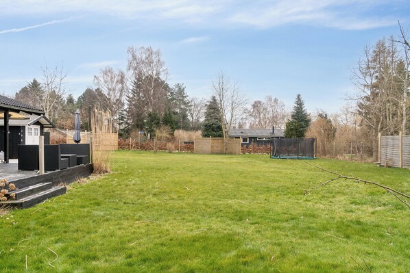 Een achtertuin met een houten terras, een trampoline en een tuinhuis.