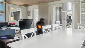 A modern kitchen with a wood-burning stove, white furniture, and a hanging light fixture.