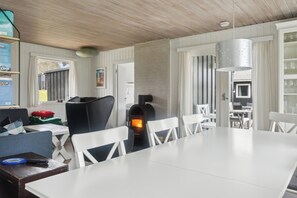 A modern kitchen with a wood-burning stove, white furniture, and a hanging light fixture.