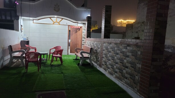 A patio area with artificial grass, outdoor furniture, and a brick wall. - 2-bedroom villa in welcoming Faridabad with WiFi, AC, badminton court within. (Faridabad)