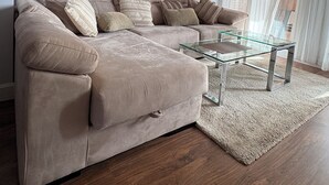 A modern living room with a beige sectional sofa, a glass coffee table, and a bull-themed painting on the wall.