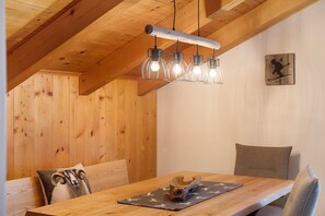 Una mesa de comedor de madera con un mantel individual, un banco de madera con cojín y una lámpara colgante con cuatro bombillas.