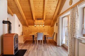 A wooden interior with a dining table, chairs, a built-in stove, and a window with curtains.