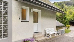 Un bâtiment à l’extérieur blanc, avec une porte d’entrée, un banc et des marches menant à l’entrée.