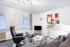 A modern living room with a black leather chair, a glass coffee table, a grey sofa, a flat-screen TV, and a potted plant. - Apartment 'Typ B' with Mountain View, Shared Terrace and Wi-Fi (Schmallenberg)