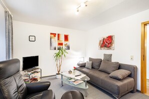 A modern living room with a sofa, armchair, coffee table, TV, and artwork on the walls. - Apartment 'Typ B' with Mountain View, Shared Terrace and Wi-Fi (Schmallenberg)