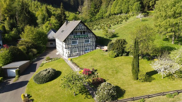 Ein traditionelles Fachwerkhäuschen mit der Aufschrift 'Haus Wald-Eck' in einem üppigen, grünen Tal, umgeben von Wald.