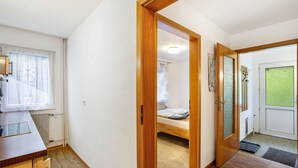Ein Zimmer mit einem Bett, einer Holztür, einem Heizkörper, einem Fenster mit Jalousien und einem kleinen Schreibtisch.