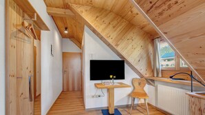 A wooden interior with a TV on a wall, a desk, a chair, and a radiator. - Room 'Lärche' with Mountain View and Wi-Fi (Bernau im Schwarzwald)