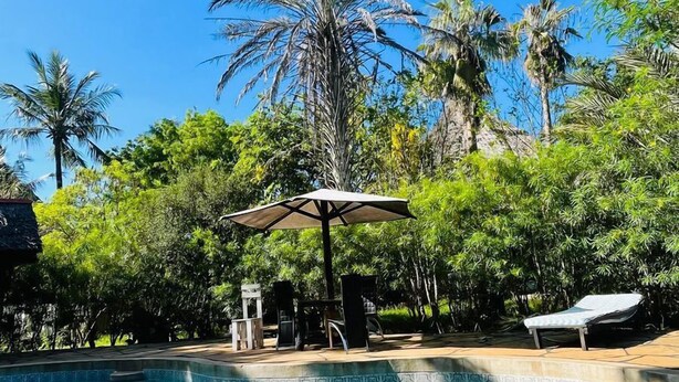 A clear blue pool surrounded by lush greenery and palm trees, with a pergola and lounge chairs. - one bedroom 8 min to the beach (Diani Beach)