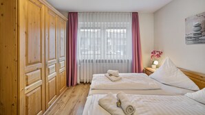 Une chambre d’hôtel avec une armoire en bois, deux lits, une table de chevet avec une lampe et un tableau au mur.