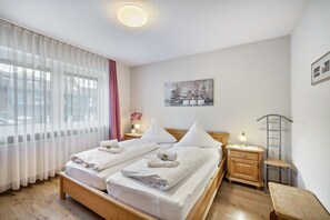 Un lit double avec du linge de lit blanc, une table de chevet avec une lampe, une petite chaise en bois et un tableau accroché au mur.