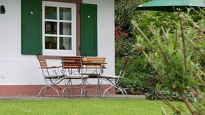 Eine Terrasse mit Tisch und Stühlen, einem grünen Sonnenschirm und einem Fenster mit Fensterläden.