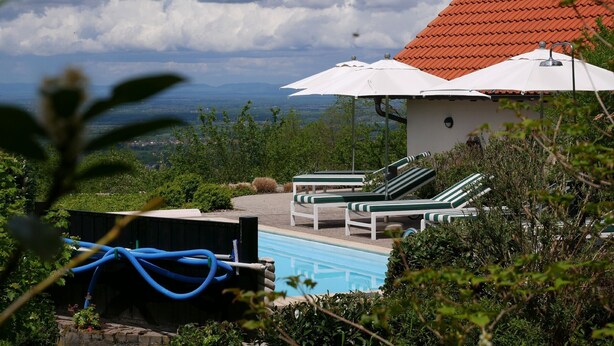 A pool area with lounge chairs and umbrellas, surrounded by greenery and a view of distant mountains. - Apartment 'Bachblick' with Shared Pool and Wi-Fi (Sasbachwalden)