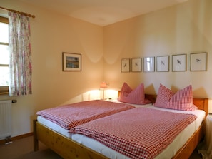 Slaapkamer met twee bedden, een radiator, een raam met bloemen gordijnen, een wandlamp en meerdere ingelijste foto's.