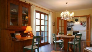 A dining area with a wooden table, chairs, a chandelier, and a kitchen in the background. - Apartment 'Bachblick' with Shared Pool and Wi-Fi (Sasbachwalden)