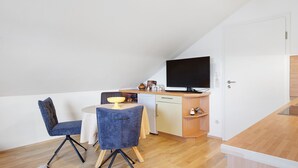 A compact kitchenette with a TV, a dining table with chairs, and a white door. - Apartment 'Eulennestle' with Shared Terrace, Balcony and Wi-Fi (Lenzkirch)