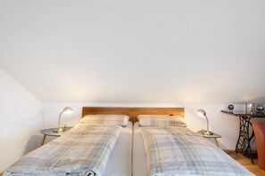Een slaapkamer met twee bedden, een houten hoofdbord, nachtkastjes met lampen, een klein tafeltje met decoratieve objecten en een stoel.