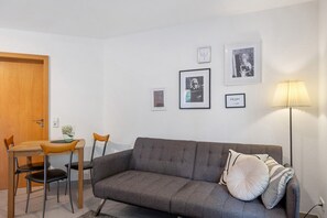 Une pièce avec un canapé gris, une table à manger en bois avec des chaises, une lampe et des tableaux encadrés accrochés au mur.