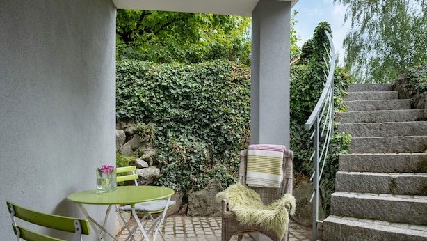 Eine Terrasse mit Tisch, Stühlen, einem Korbsessel mit Felldecke und einer Steintreppe.