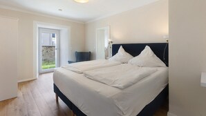 Quarto com duas camas, uma porta que dá para uma varanda e uma mesa de cabeceira com abajur.