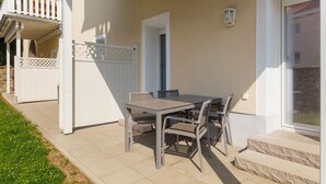 Une terrasse extérieure avec une table et des chaises, une clôture blanche et une porte donnant accès à un bâtiment.