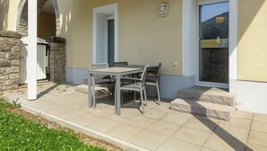 Un patio con una mesa y sillas, un arco de piedra, una puerta blanca y una ventana con vistas a una colina.