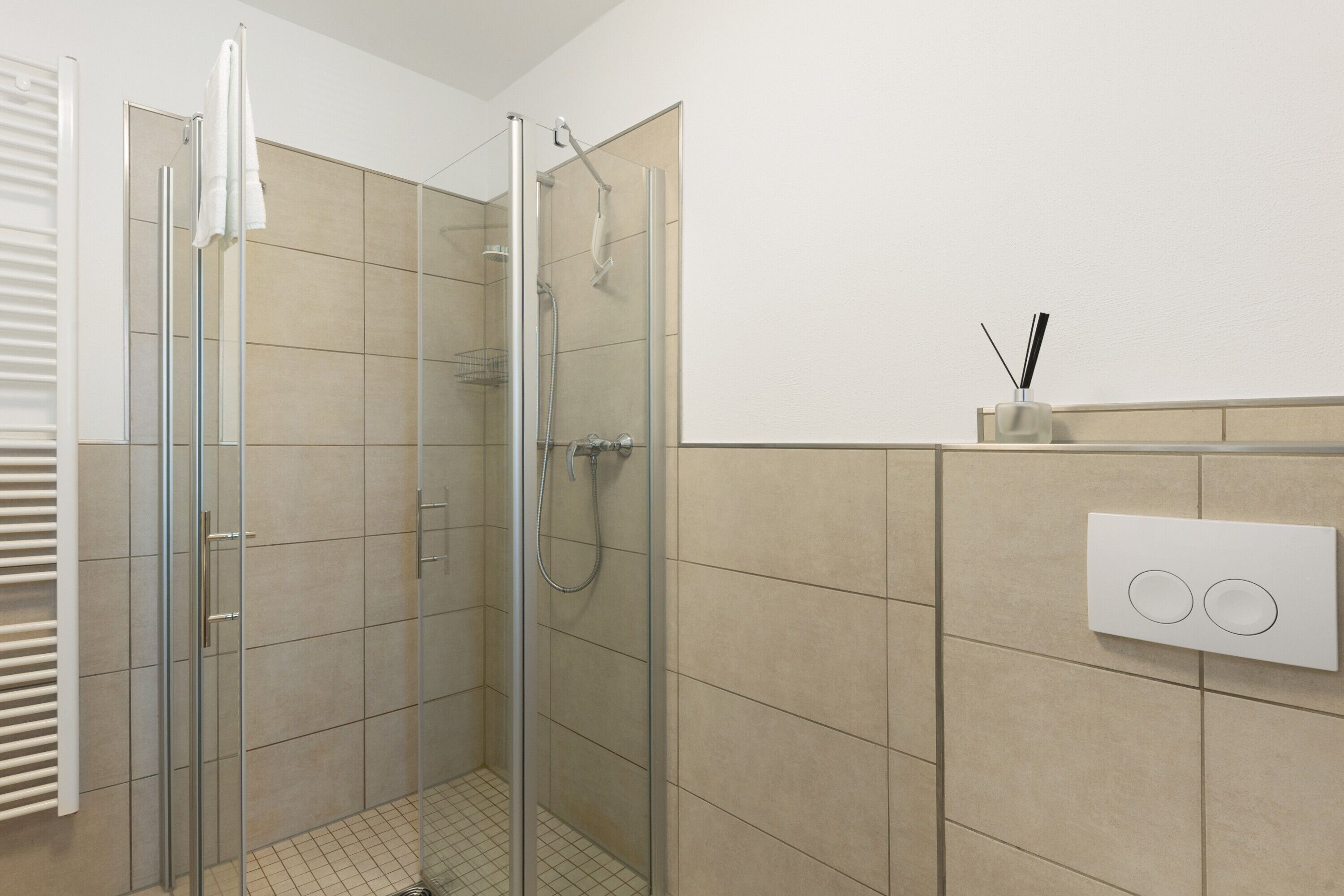 Une douche en verre avec un pommeau de douche à main, un porte-serviettes et un interrupteur fixé au mur.