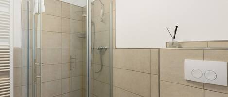 Une douche en verre avec un pommeau de douche à main, un porte-serviettes et un interrupteur fixé au mur.