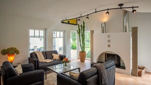 A modern living room with a fireplace, leather sofas, a glass coffee table, and a large potted plant. - Holiday Home 'Wennetraum' with Sauna, Terrace, and Garden (All for Private Use!) (Eslohe)