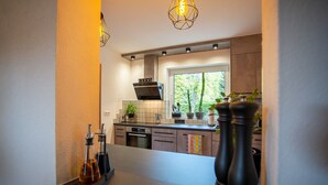 A modern kitchen with a built-in oven, a window with a view of greenery, and a countertop with kitchen utensils. - Holiday Home 'Wennetraum' with Sauna, Terrace, and Garden (All for Private Use!) (Eslohe)