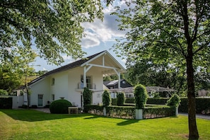 Una casa bianca a due piani con un portico coperto, circondata da siepi curate e alberi.