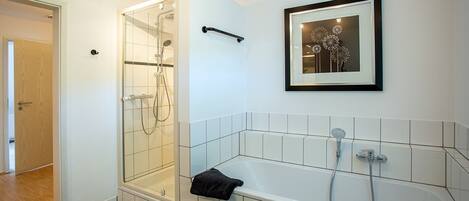 A bathroom with a shower, a bathtub, and a framed artwork on the wall.