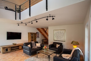 Un'ampia zona giorno con soffitto alto, una scala e una televisione a schermo piatto.
