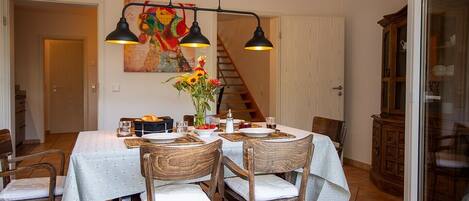 Un comedor con una mesa preparada para cuatro, sillas, un cuadro en la pared y una escalera al fondo.